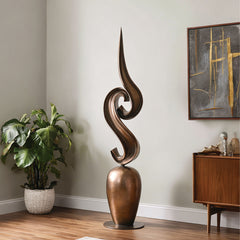 An abstract fluid bronze s-curve sculpture in a room has wooden floors and natural daylight.