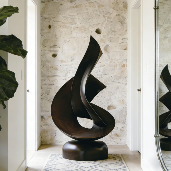 Abstract Embracing Swirl Bronze sculpture in a room with stone wall and plant