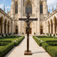 Statue of Christ on the Cross Bronze Sculpture centered in a formal garden courtyard leading up to a grand stone cathedral.