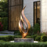Abstract large dancing flame bronze sculpture in a garden setting with a building in the background