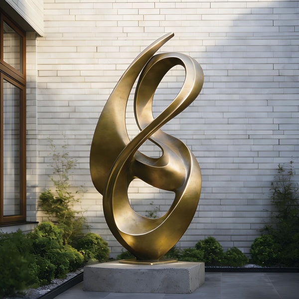 Abstract flowing gold bronze sculpture on a pedestal in front of a light gray brick wall.