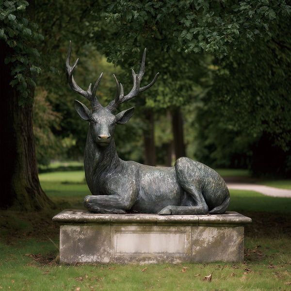 Bronze statue of a resting deer with large antlers in a park setting