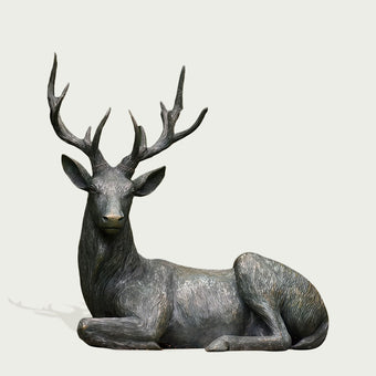 Bronze statue of a resting deer with large antlers on a light gray background