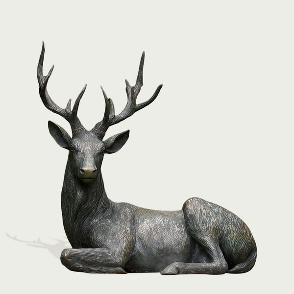 Bronze statue of a resting deer with large antlers on a light gray background
