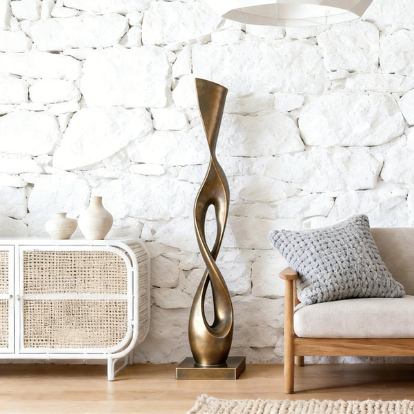 Abstract Graceful Twist Bronze sculpture in a living room with a textured white wall and furniture.