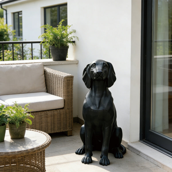 Black bronze dog statue on a patio with a couch, table, and plants.