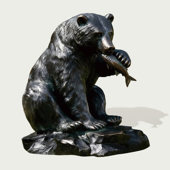 Bronze statue of a bear holding a fish on a white background