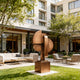 Contemporary Abstract  Bronze Geometric Sculpture Arcus Stamp chairs, and tables in front of a building.