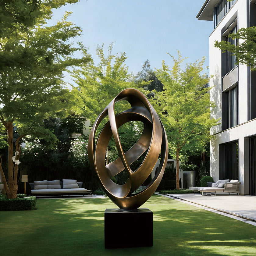 Continuous Interlocking Ribbon Abstract Bronze Sculpture on a black pedestal base, set in a modern outdoor courtyard with green grass, trees, and contemporary white buildings.