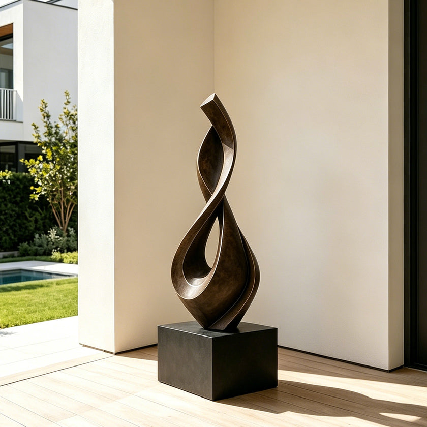 Fluid Twisting Infinity Teardrop Bronze Landscape Sculptures with a flowing, intertwined looped form mounted on a black rectangular pedestal, displayed in a modern interior space with light wood flooring and a sunlit cream wall.