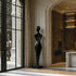 Graceful Female Silhouette Glossy Black Bronze Sculpture stands on a matching base in a modern interior hallway with arched entryways, warm wood cabinetry, and large windows.