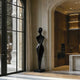 Graceful Female Silhouette Glossy Black Bronze Sculpture stands on a matching base in a modern interior hallway with arched entryways, warm wood cabinetry, and large windows.