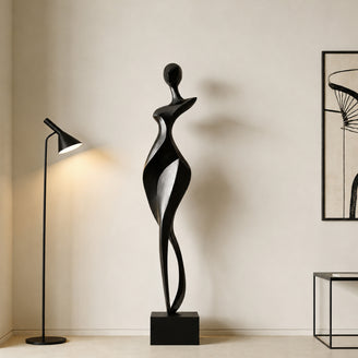 Rhythmic Walking Woman Abstract Bronze Figure Sculpture of a stylized female figure standing on a rectangular black marble base, displayed in a minimalist room next to a lit floor lamp and a framed abstract print.