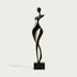 Rhythmic Walking Woman Abstract Bronze Figure Sculpture of a stylized female figure standing on a rectangular black marble base, set against a light gray background.