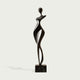 Rhythmic Walking Woman Abstract Bronze Figure Sculpture of a stylized female figure standing on a rectangular black marble base, set against a light gray background.