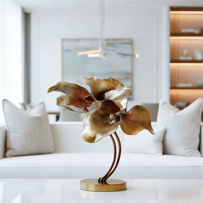 Graceful Lily Leaves Metal Art Home Decor Bronze Statues with textured, layered petals on a curved stem and round base, displayed on a white table in a modern living room setting.