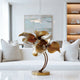 Graceful Lily Leaves Metal Art Home Decor Bronze Statues with textured, layered petals on a curved stem and round base, displayed on a white table in a modern living room setting.