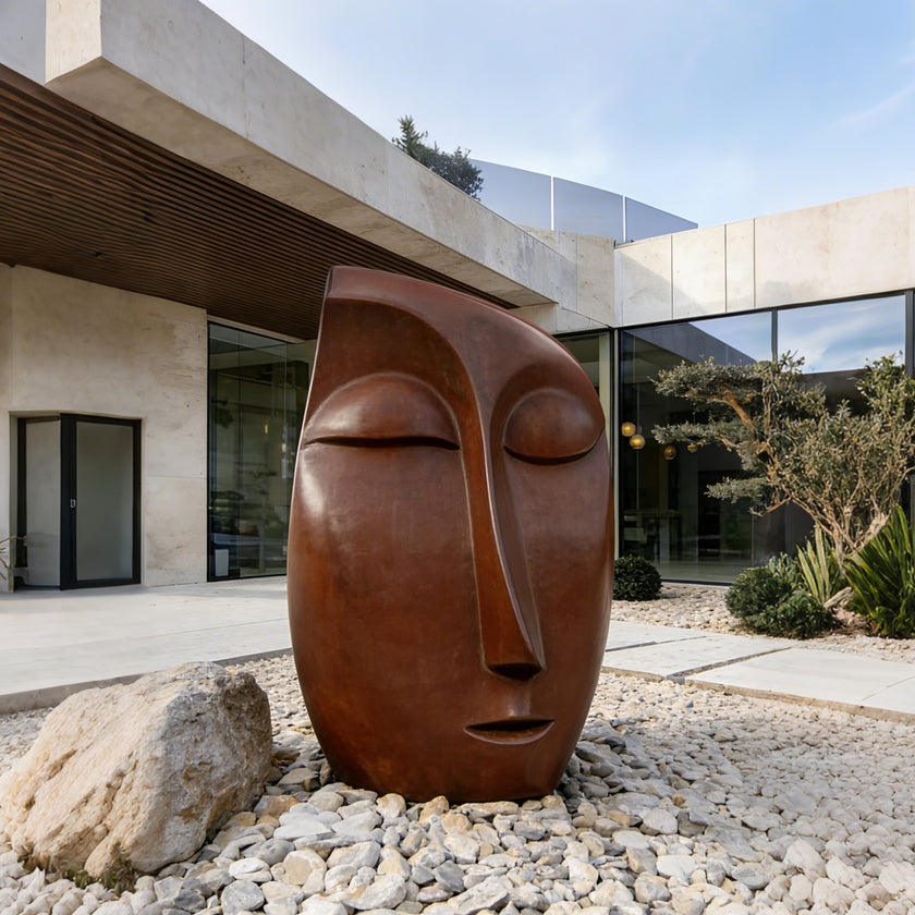 Serene Meditative Face Abstract Bronze Sculpture of a stylized face with closed eyes, set outdoors on a bed of white gravel in front of a modern concrete and glass building.