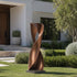 Twisted Hourglass Abstract Contemporary Bronze Sculpture on a square base, displayed on a green lawn in front of a modern house.