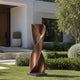 Twisted Hourglass Abstract Contemporary Bronze Sculpture on a square base, displayed on a green lawn in front of a modern house.