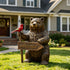Rustic Welcoming Bear With Bird Bronze Garden Statues Garden Animal Statues standing on a lawn in front of a house, holding a wooden welcome sign and perched on a red bird, photographed in a real outdoor setting.