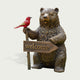 Rustic Welcoming Bear With Bird Bronze Garden Statues Garden Animal Statues holding a wooden welcome sign, with a bright red bird perched on the signpost, shown against a plain light background.