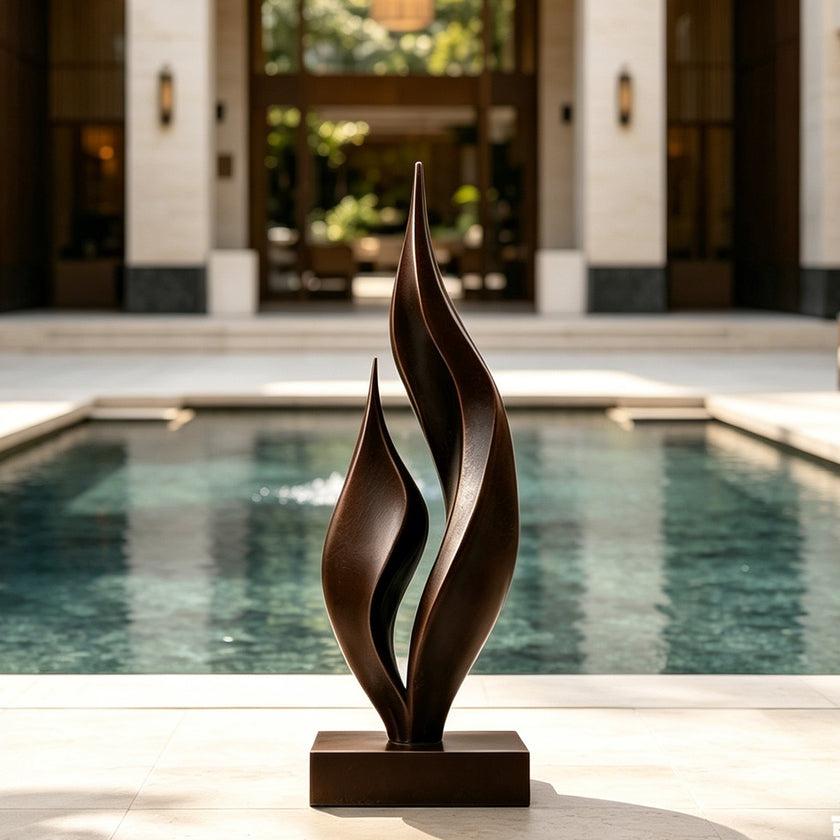 Dancing Twin Flames Bronze Art Sculpture with two tall, flowing leaf-like forms on a rectangular base, placed in front of a swimming pool in a luxurious outdoor courtyard.