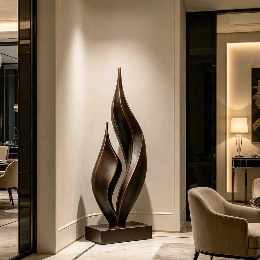 Dancing Twin Flames Bronze Art Sculpture with two flowing, flame-like vertical forms standing on a rectangular base in a warmly lit interior hallway.