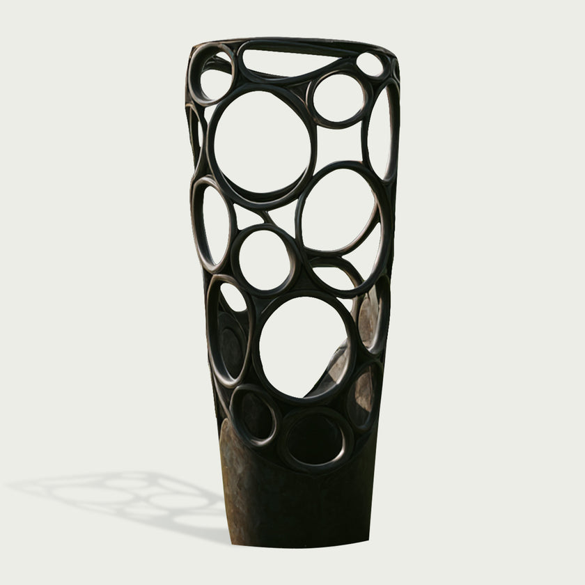 Freestanding abstract bronze sculpture featuring an elongated column form, interconnected organic circular openings, smooth rounded edges, and a dark bronze patina.