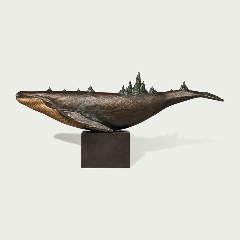 Surreal bronze whale sculpture featuring an elongated swimming form, finely textured body, detailed ventral grooves, and miniature mountain-like ridges rising along its back, displayed on a dark rectangular pedestal.
