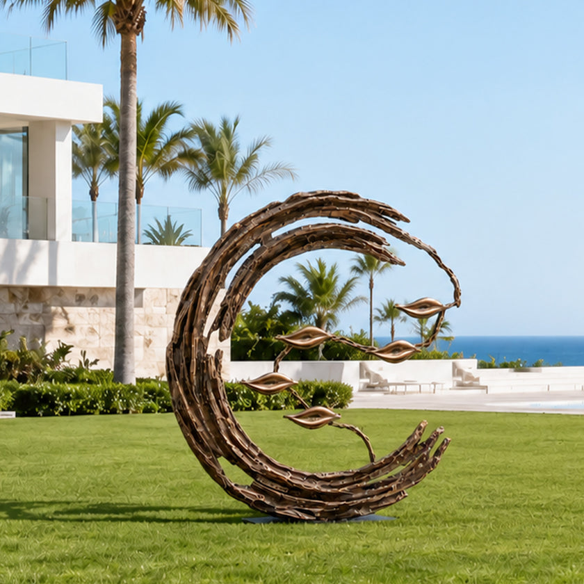 Abstract bronze crescent garden sculpture installed on a green lawn at a coastal villa, with textured sweeping branches and delicate floating leaves framed by palm trees, modern architecture, and an ocean view.