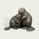 Bronze beaver pair sculpture depicting two affectionate beavers sitting closely together, with one gently embracing the other, detailed textured fur, broad patterned tails, expressive faces, and natural green patina accents over warm bronze.