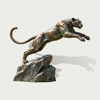 Life-size bronze leaping panther sculpture captured in a powerful forward jump, with a muscular streamlined body, outstretched paws, curved tail, realistic feline features, and a textured rocky base with verdigris detailing.