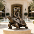 Whimsical bronze sculpture of a smiling boy wearing a cap and backpack while sitting on a giant tortoise, displayed on a circular stone pedestal beside a luxury courtyard fountain.