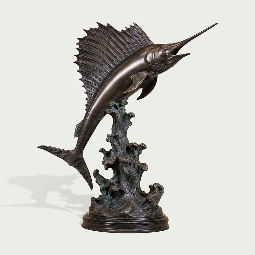 Large bronze sailfish sculpture in a dramatic upward leaping pose, featuring an elongated bill, open mouth, tall ribbed dorsal fin, detailed fins and tail, and a sculpted ocean-wave base with subtle verdigris accents.