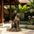 Large bronze seated panther sculpture beside a tropical resort pool, featuring a poised upright posture, muscular body, curled tail, realistic feline face, and warm bronze patina on a natural rock-style base.