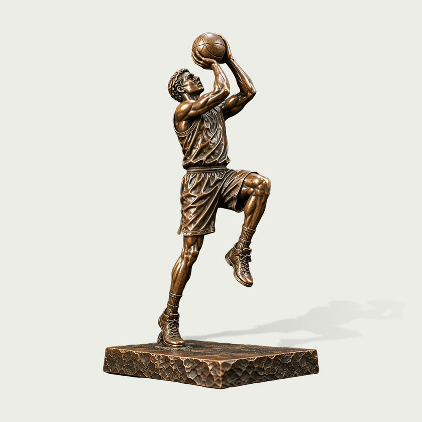 Bronze basketball player sculpture depicting an athlete rising for a jump shot, with both hands holding the ball, one knee raised, detailed sportswear, muscular anatomy, and a textured rectangular base.