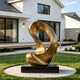 Large abstract bronze sculpture with an elegant continuous loop and fluid organic curves, displayed on a black pedestal in the landscaped garden of a modern luxury residence.