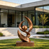 Large contemporary abstract bronze sculpture featuring sweeping flame-like curves surrounding a suspended sphere, displayed on a bronze pedestal in the landscaped garden of a modern luxury residence.