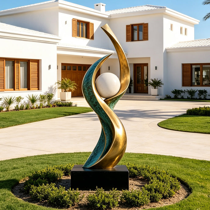 Large outdoor abstract bronze sculpture with flowing green patina and golden curves surrounding a white sphere, installed on a black pedestal in the landscaped front garden of a modern luxury villa.