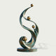 Front product view of an abstract bronze sculpture featuring elegant S-shaped verdigris ribbons, multiple polished golden spheres, and a round bronze base.