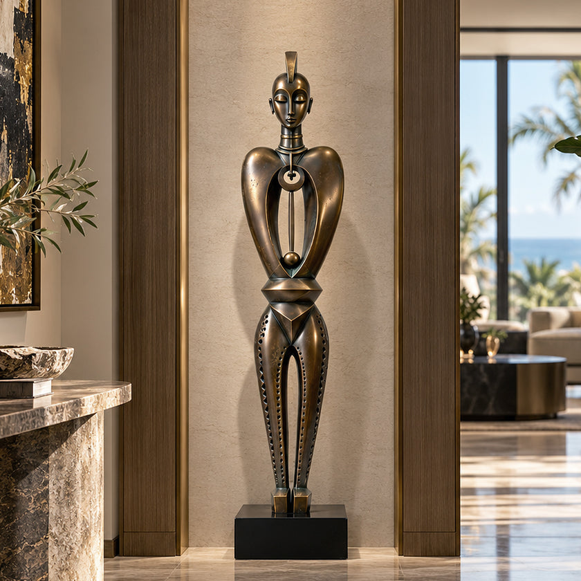 A tall, abstract geometric tribal figure bronze floor sculpture displayed in a luxury living room. This slender art piece features a stylized face and a hollow torso with a dangling sphere. The dark metallic finish adds cultural depth to the modern indoor space.