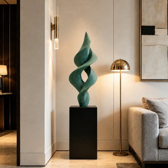 A twisting, abstract green sculpture on a black pedestal in a modern interior, placed beside a brass floor lamp and a grey sofa