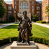 A classic bronze figure statue of Apostle Paul holding a sword and book while pointing upward. This highly detailed religious metal art piece is beautifully displayed outdoors on a lawn in front of a historic red brick academic building.