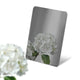 Stainless steel color sample mirror polished black sheet with a reflection of white flower on a white background
