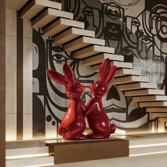 Dynamic Red Fiberglass Holding Hands Rabbit Pair on a wooden platform with a modern wall design in the background.