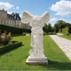 Classic Greek Winged Victory Of Samothrace Marble Statue Replica in a garden with a castle in the background