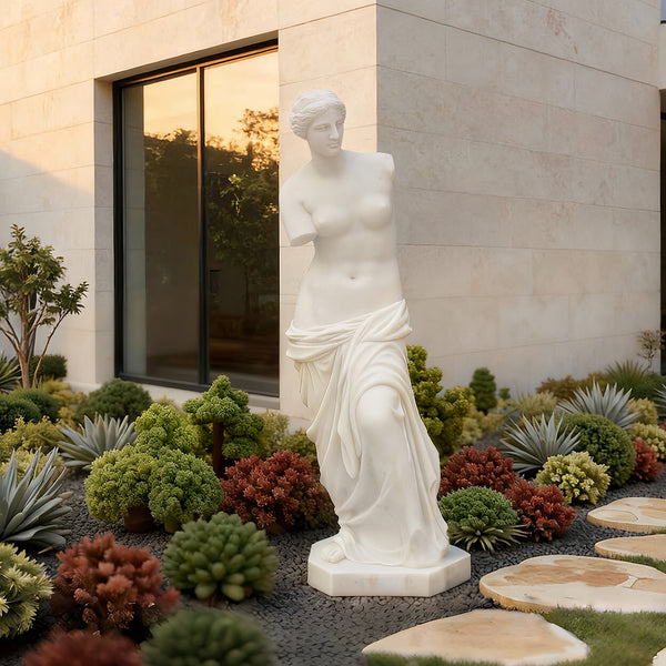 Venus de milo greek goddess sculpture replica  in a garden setting with a building in the background