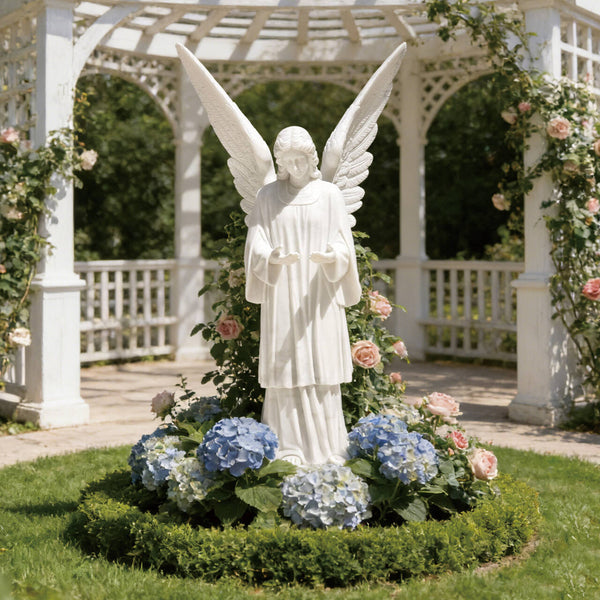 Large cathedral angel statue in a garden with flowers and a white gazebo in the background