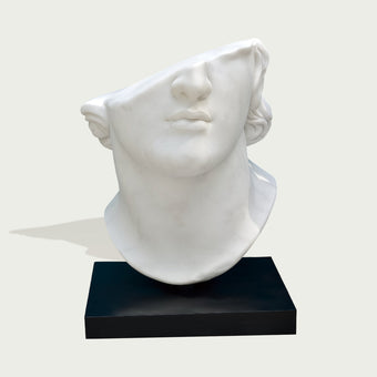 fragmented marble bust head sculpture on a black base against a light gray background